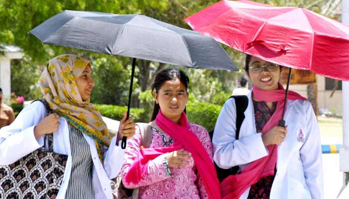 Medical students walk under an umbrella to protect themselves from intense heat and direct sunlight during hot weather at LUMHS Jamshoro.— APP