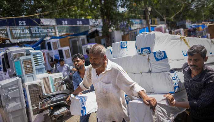 Labourers use a cart to transport aluminium pipes at a market on a hot summer day in New Delhi, India. — Reuters/File