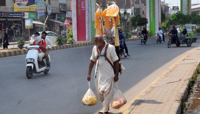 An elderly street vendor walks along a busy road carrying snacks and goods on his shoulders, heading toward customers amid the city’s daily hustle, Multan, May 2, 2026. — APP