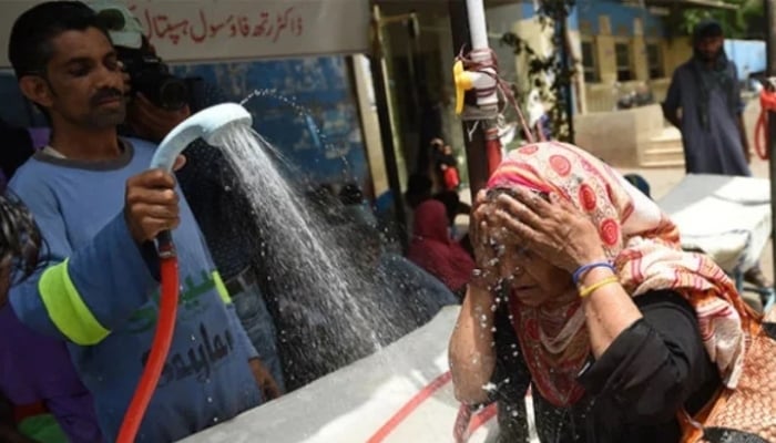 A volunteer showers a woman with water during a heatwave in Karachi. — AFP/File