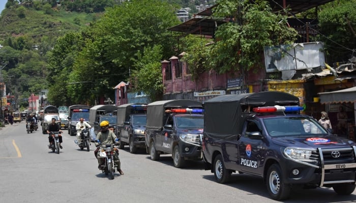 Commuters ride past security personnel as they patrol a street ahead of a protest by the banned Joint Awami Action Committee (JAAC) in Muzaffarabad, Azad Jammu and Kashmir on June 7, 2026. — AFP