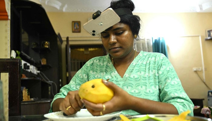 An Indian housewife Nagireddy Sriramyachandra wearing a smartphone on her head as she records her actions through motion capture while slicing mangoes at her home in Chennai. — AFP