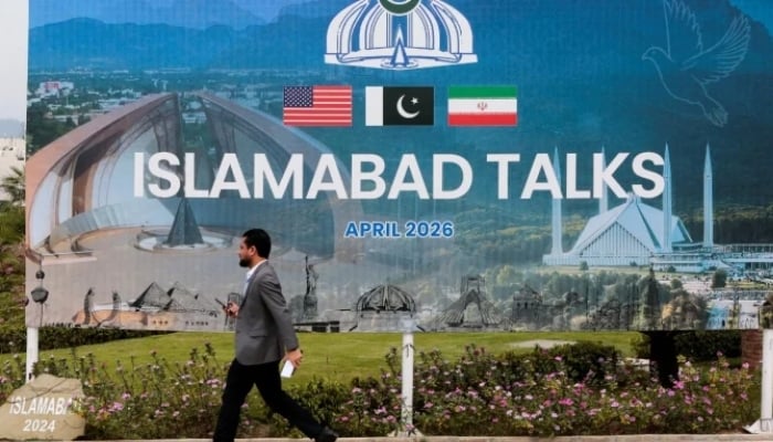 A man walks past a billboard near the media centre as delegations from the United States and Iran are expected to hold peace talks in Islamabad, on April 11, 2026. — Reuters
