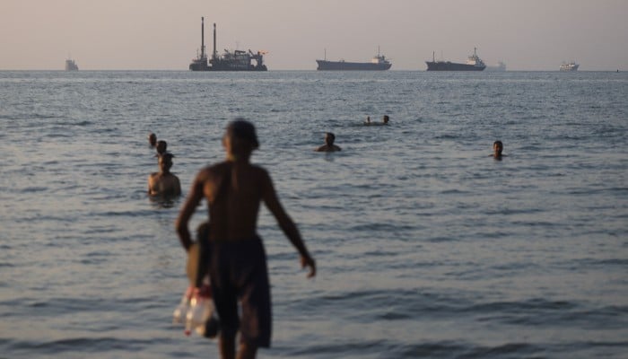 In this picture obtained from Irans ISNA news agency on June 8, 2026, residents take a dip as cargo and commercial vessels lie at anchor in the Strait of Hormuz off Bandar Abbas. — AFP
