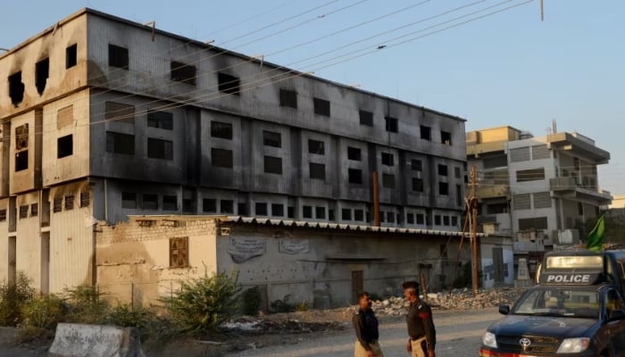 Policemen stand in front of the burnt out Baldia Town factory in Karachi in this undated photo. — AFP/File