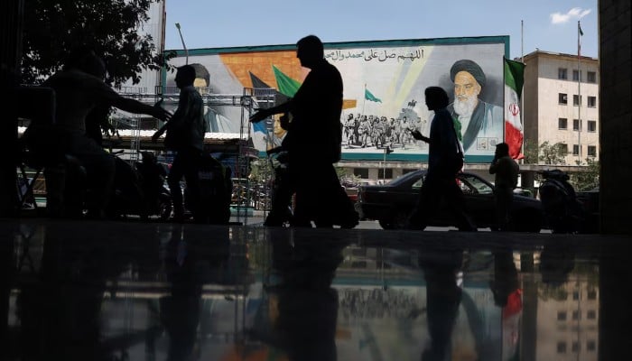 People walk near a mural depicting the late leader of the Islamic Revolution, Ayatollah Ruhollah Khomeini, and Irans late Supreme Leader Ayatollah Ali Khamenei, on a street in Tehran, Iran, June 14, 2026.