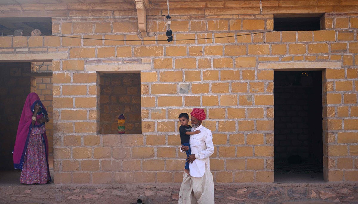 Image shows herdsman Sawai Singh Bhatis father, Khet Singh carrying his grandson at their house in Sanwata village on the outskirts of Rajasthans Jaisalmer city.— AFP