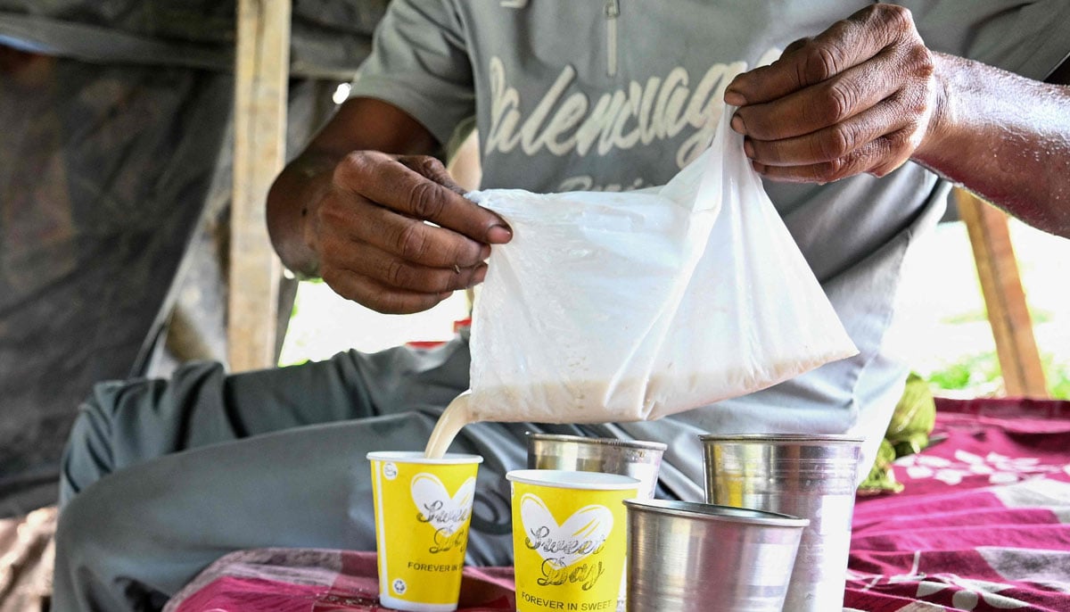 Farmer Bhole Shankar pouring fruit juice after returning from work in approximately 40 degrees Celsius temperatures, inside his shanty on the Yamuna river floodplains in New Delhi.— AFP