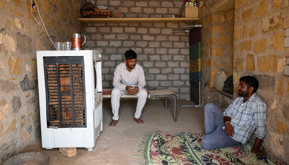 Herdsman Sawai Singh Bhati (left) talks to his brother while sitting in front of an air-cooler in 42℃ temperatures, at his house in Sanwata village on the outskirts of Rajasthan´s Jaisalmer city. — AFP