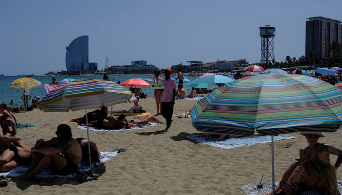 A man sells drinks for tourists and locals as they enjoy the Barceloneta beach as temperatures rise, during a heatwave affecting a large part of Spain, in Barcelona, Spain, June 21, 2026.  — Reuters