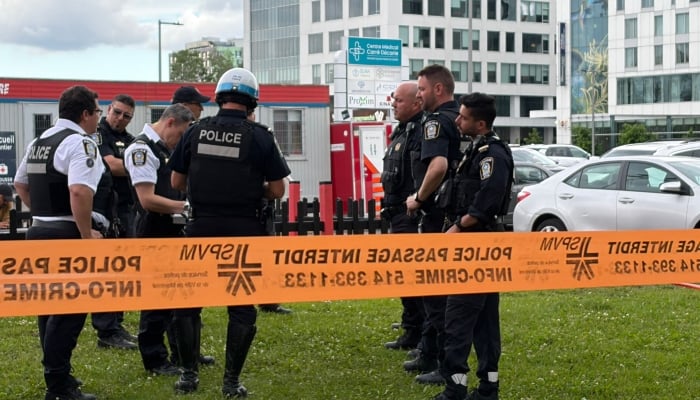 Damaged windows can be seen in the distance (top C) as police gather near the scene of a shooting in Montreal on June 22, 2026. — AFP