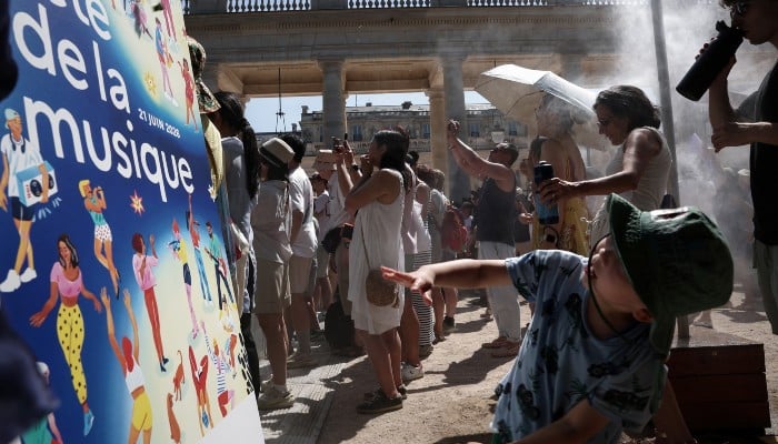 Pedestrians cool off under a mist sprayer installed by Paris City Hall on the 45th edition of the Fête de la Musique (Frances national music festival) and during a heatwave on June 21, 2026. — AFP