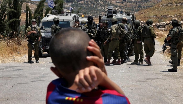 Israel targeted Gaza children resulting in genocide: UN inquiry 11 A Palestinian boy looks on as Israeli security forces stand guard before Palestinians gathering to protest threats of confiscation of their land in the Palestinian village of Idna, west of Hebron in the occupied West Bank, on June 12, 2026. — AFP
