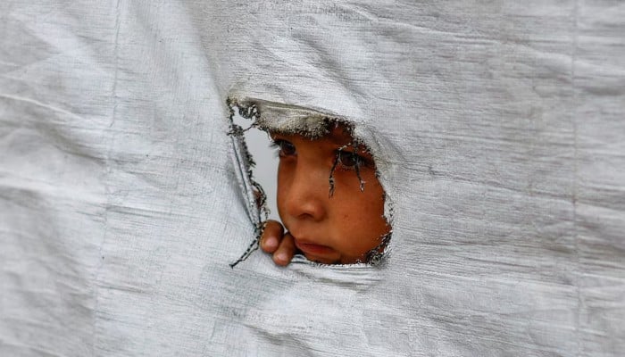 A displaced Palestinian boy peers through a tear in a tent wall, in Gaza City, May 6, 2026. — Reuters