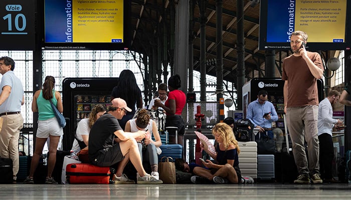 Passengers wait for their train on June 22, 2026 at the Gare du Nord in Paris, using a fan and a hand fan under the SNCF information panels about the heatwave. — AFP