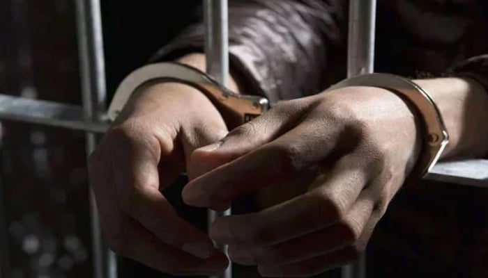A representational image of a handcuffed man standing behind bars. — APP/File