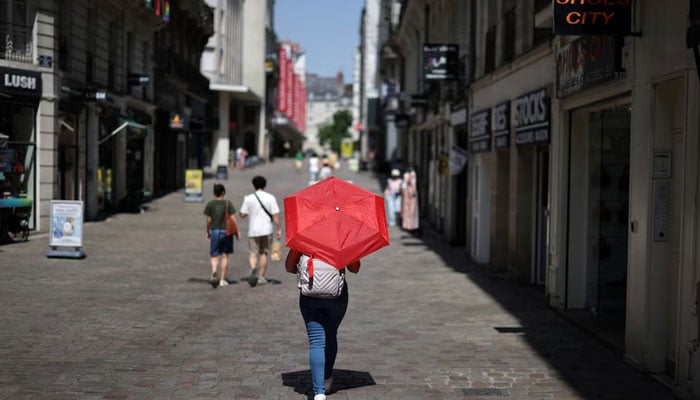 A woman uses a red umbrella to shade from the sun while walking on a street in Nantes as temperatures rise during a heatwave affecting a large part of France, June 22, 2026. — Reuters