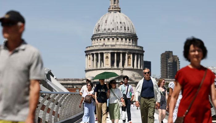 A couple walks with an umbrella along the Millennium Bridge as Britain experiences record temperatures disrupting schools and transport networks in London, Britain, June 23, 2026. — Reuters