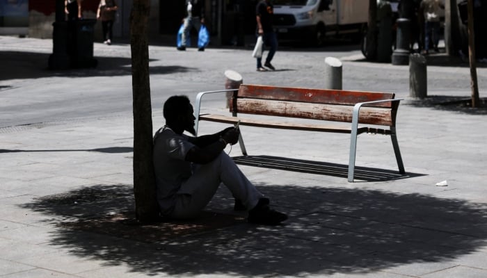 A man sits in the shade of a tree to escape the heat during a heatwave in Madrid, Spain, June 23, 2026. — Reuters