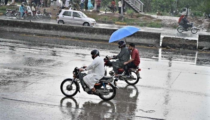 A motorcyclist on the way under cover on an umbrella at IJP Road during rain in Islamabad, June 22, 2026. — APP