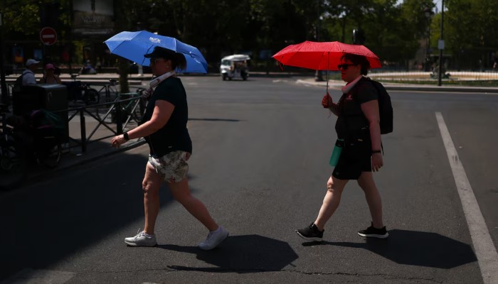 People cross the road whilst taking shelter under umbrellas in central Paris during high temperatures amid a heatwave in Paris, France, June 27, 2026. — Reuters