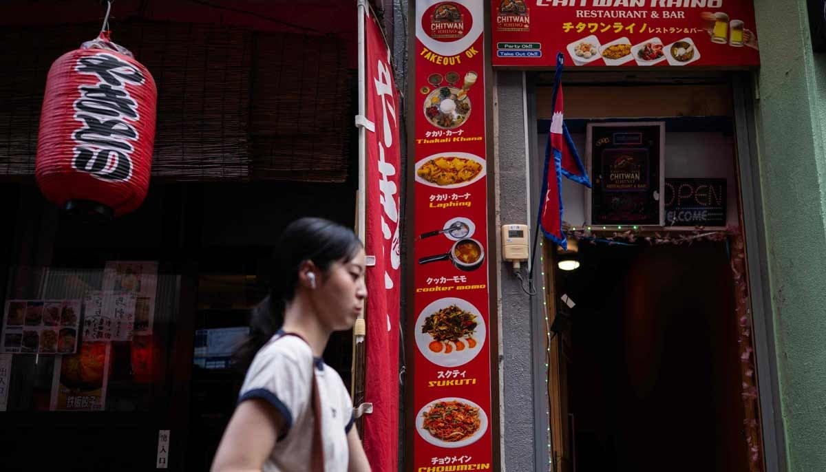 A woman passes a Japanese restaurant and the Chitwan Rhino Restaurant and Bar in the Okubo Shin area, one stop north of Shinjuku metro, in Tokyo on June 12, 2026. — AFP