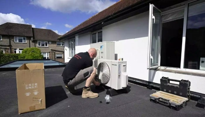 An engineer installs an air conditioning unit on the roof of a residential home in Croydon, south London, on July 1, 2026. — AFP