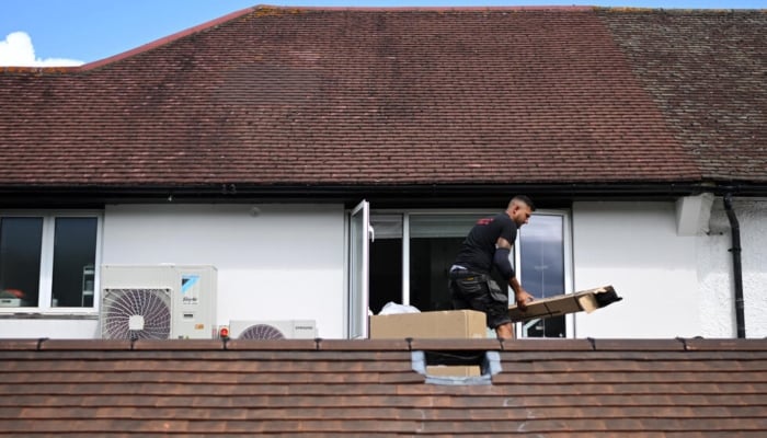 An engineer installs an air conditioning unit on the roof of a residential home in Croydon, south London, on July 1, 2026. — AFP
