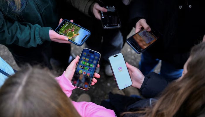 Teenagers pose for a picture while looking at their phones, in Bonn, Germany, February 20, 2026.— Reuters