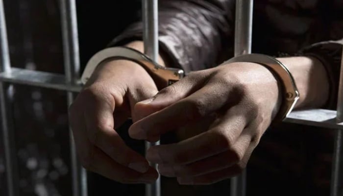 A representational image of a handcuffed man standing behind bars. — APP/File