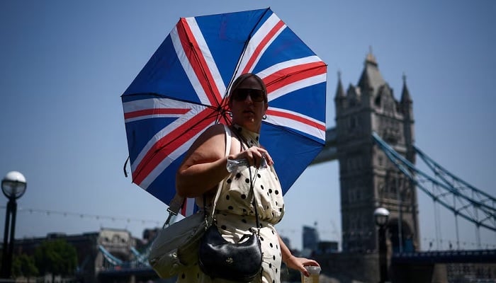 A woman uses an umbrella to shield herself from the sun while walking near Tower Bridge, amid a heatwave, as Britain experiences record temperatures disrupting schools and transport networks, in London, Britain, June 25, 2026.— Reuters