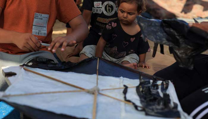 A child looks on as Palestinians make a kite at a tent camp sheltering displaced people in Gaza City, August 25, 2026. — Reuters