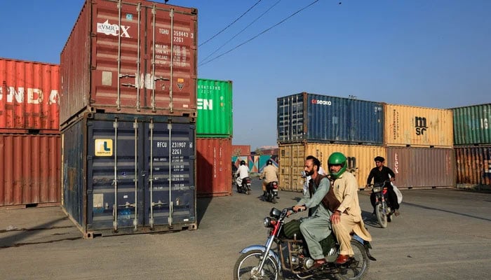 This representational image shows people ride past shipping containers on a road leading to the US Consulate General in Karachi, on March 2, 2026. — Reuters