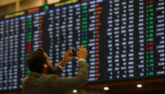 A man uses a mobile phone as he takes a photo of the electronic board displaying share prices during a trading session at the Pakistan Stock Exchange, in Karachi on November 28, 2023. — Reuters