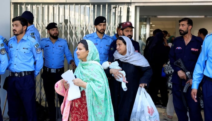 A woman carrying an infant moves past police officers as she leaves a ward following a deadly fire at the Pakistan Institute of Medical Sciences hospital in Islamabad, August 26, 2026. — Reuters