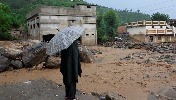 A resident stands with an umbrela as rain water flowing from mountains crosses a damaged area, following a storm that caused heavy rains and flooding in Bayshonai Kalay, Buner district, Khyber Pakhtunkhwa, August 18, 2025. — Reuters