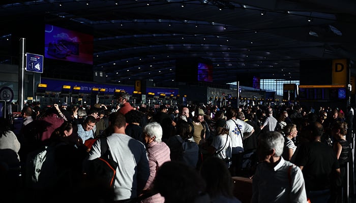People stand with their luggage as the queue at check-in desks inside Terminal 5 of London Heathrow airport, west of London on September 8, 2026, following major disruption due an issue affecting the Nats air traffic control systems. — AFP