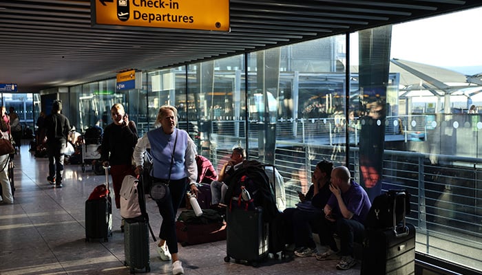 People sit on the floor with their luggage inside Terminal 5 of London Heathrow airport, west of London on September 8, 2026, following major disruption due an issue affecting the Nats air traffic control systems. — AFP