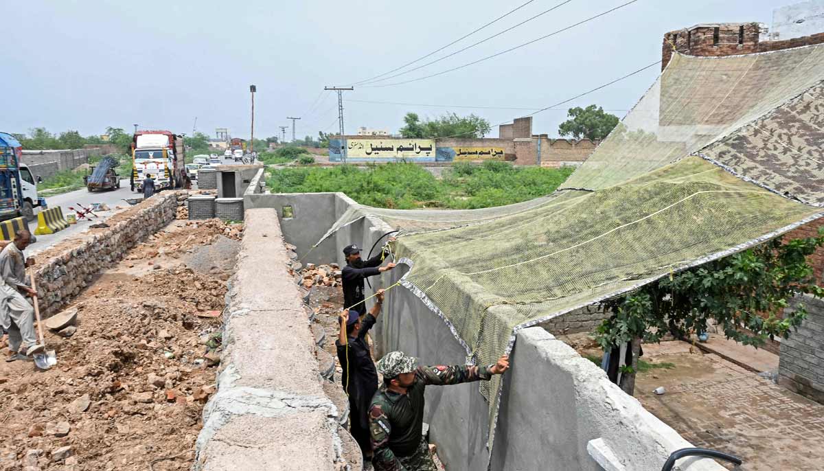 A security personnel fortifying a police post with Ukraine-style mesh barriers while a worker constructs a boundary wall, as a new line of defence against militant drone and aerial attacks in Khyber Pakhtunkhwa.— AFP