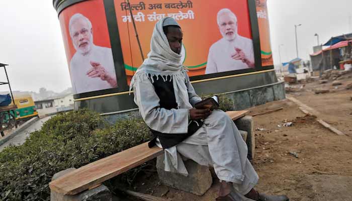 A Muslim man reads the Holy Quran as he sits in front of a billboard featuring Indias Prime Minister Narendra Modi in New Delhi. — Reuters/File