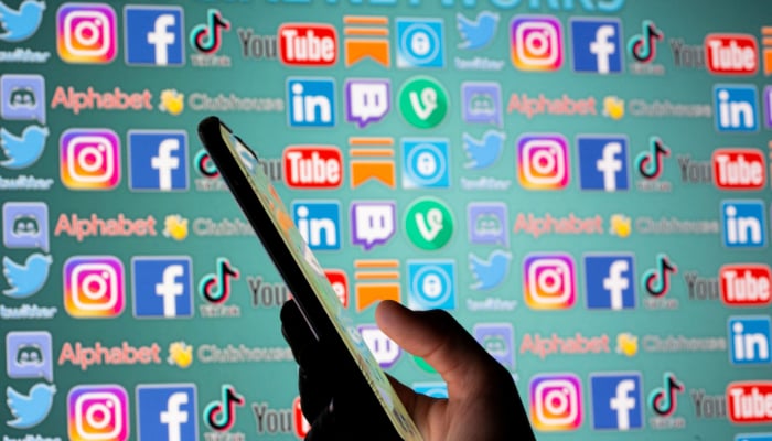 Woman with smartphone is seen in front of displayed social media logos in this illustration taken, May 25, 2021. — Reuters