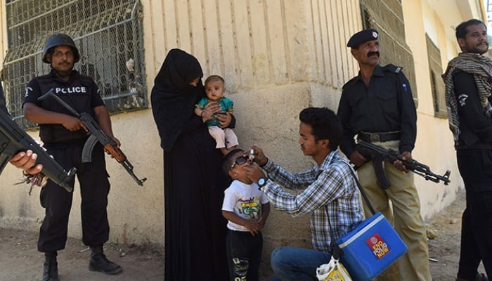 This representational image shows policemen stand guard as a health worker administers polio drops to a child during a polio vaccination campaign in Karachi. ─ AFP/File