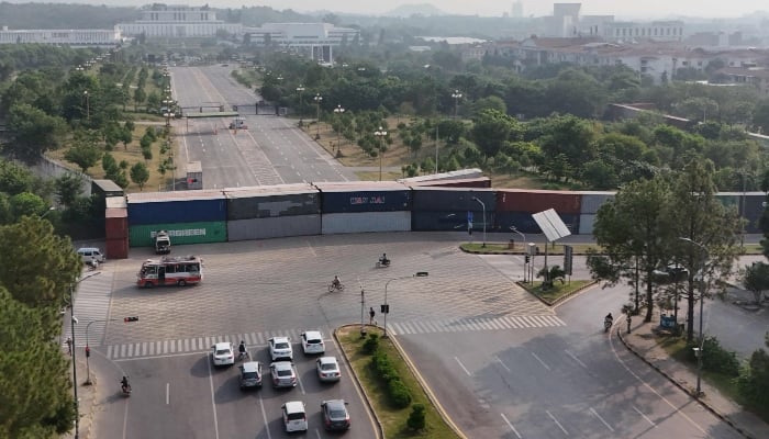 This aerial photograph shows commuters driving past shipping containers placed by authorities to block access towards the Presidents House and the Red Zone area in Islamabad on September 24, 2026. — AFP