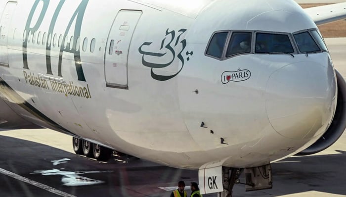 Ground staff stand next to the Pakistan International Airline (PIA) aircraft ahead of its takeoff for Paris at the Islamabad International Airport on Jan 10, 2025. — AFP