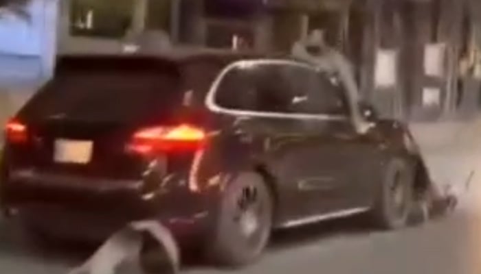 A motorcyclist is seen on the bonnet of a moving car after his motorcycle is dragged along the road in Rawalpindi. — Screengrab via X/@S_SajidOfficial