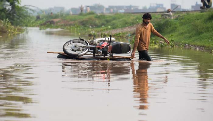 A man pulls his motorcycle across a wooden plank through floodwaters following monsoon rains in Ferozwala on July 30, 2026. — Reuters