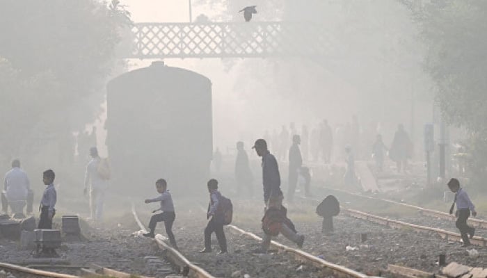 People walk across a railway track amid smoggy conditions in Lahore. — AFP/File