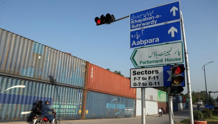 A man on motorbike rides past shipping containers used to block the area in the background, ahead of a planned march by Pakistan Tehreek-e-Insaf (PTI), in Islamabad, September 30, 2026. — Reuters