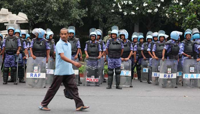 A man walks past members of the Rapid Action Force (RAF) standing guard ahead of a protest planned by the Cockroach Janta Party (CJP) seeking the resignation of Indias Chief Election Commissioner Gyanesh Kumar, near the protest site in New Delhi, India, October 10, 2026. — Reuters