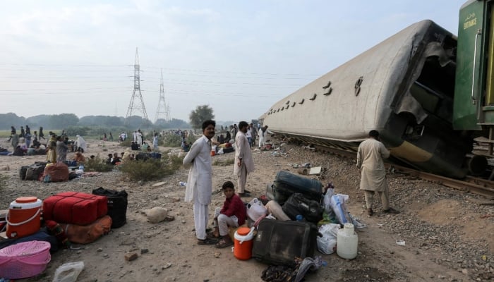 Passengers sit with their belongings next to derailed coaches of the passenger train Rehman Baba Express on the outskirts of Multan, October 13, 2026. — AFP